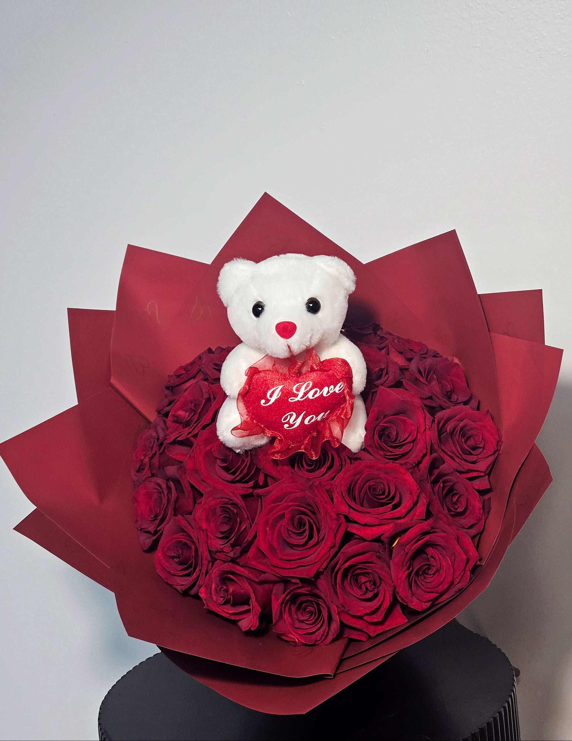 Bouquet of red roses with a white teddy bear holding a 'I Love You' heart on a white background